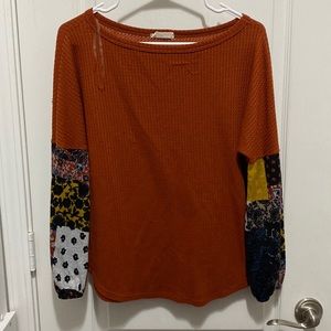 An burnt orange long sleeve sweater with patterns on the sleeves